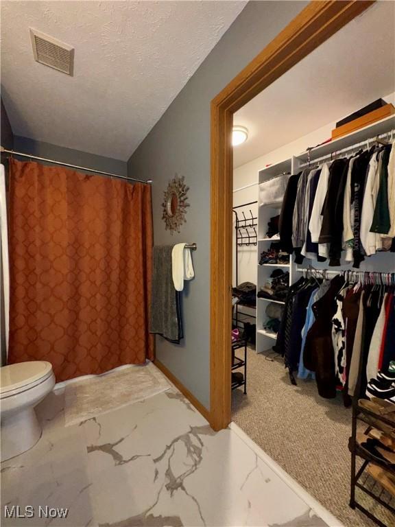 full bath with toilet, a textured ceiling, marble finish floor, a shower with curtain, and visible vents