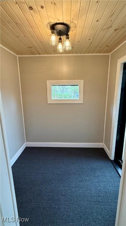 empty room with wood ceiling, baseboards, and dark carpet