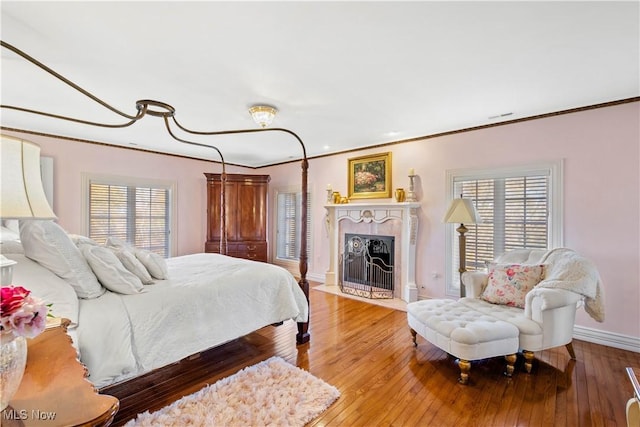 bedroom featuring a fireplace with flush hearth, baseboards, ornamental molding, and hardwood / wood-style flooring
