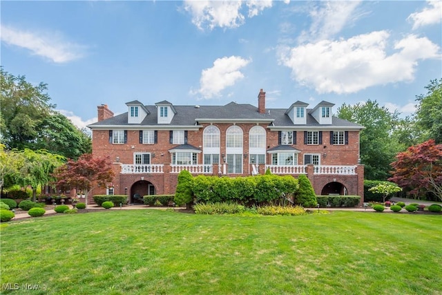 view of front facade with brick siding, a front yard, and a chimney