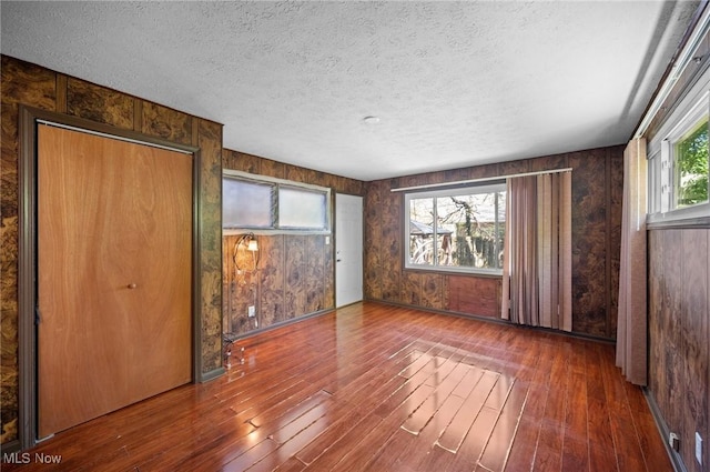 interior space featuring wood-type flooring, wooden walls, and a textured ceiling