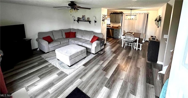 living room featuring dark wood-style flooring, a ceiling fan, baseboards, and a textured ceiling
