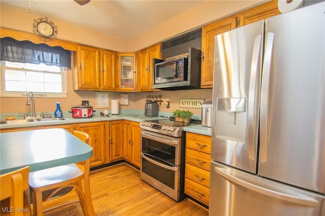 kitchen with a sink, light countertops, brown cabinetry, stainless steel appliances, and light wood-type flooring
