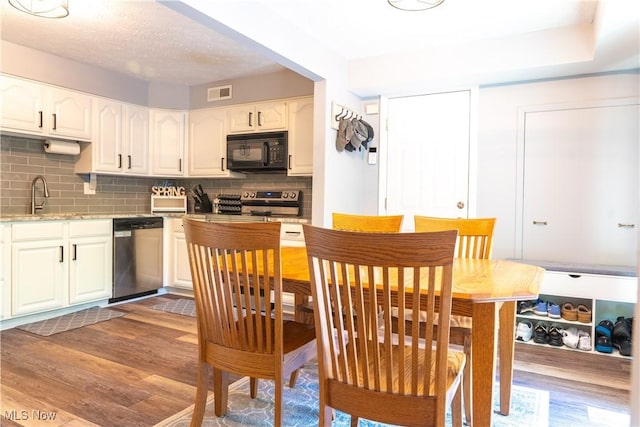 kitchen with decorative backsplash, visible vents, wood finished floors, a sink, and stainless steel appliances