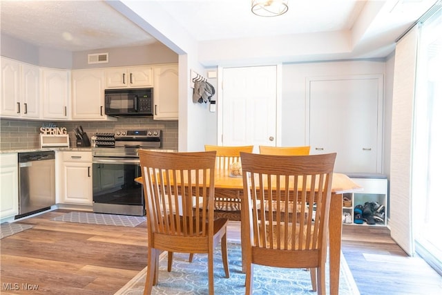 kitchen featuring visible vents, decorative backsplash, white cabinets, light wood-style flooring, and appliances with stainless steel finishes