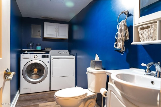 half bath featuring wood finished floors, toilet, electric panel, washing machine and clothes dryer, and a sink