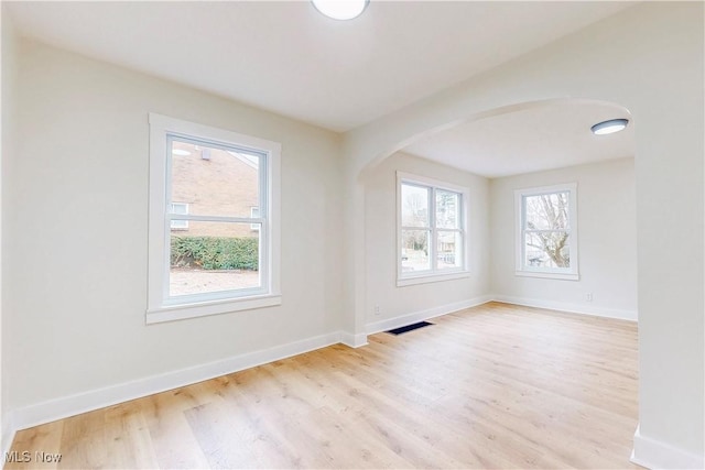 empty room with baseboards, arched walkways, wood finished floors, and visible vents
