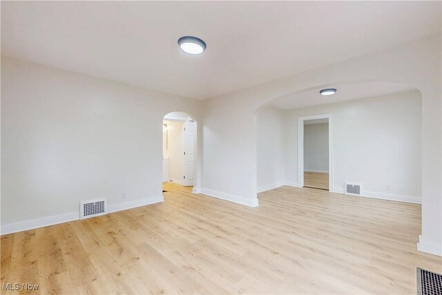 unfurnished room featuring visible vents, arched walkways, and light wood-type flooring