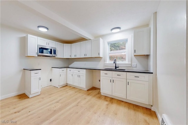 kitchen with a sink, light wood-style flooring, stainless steel microwave, and dark countertops
