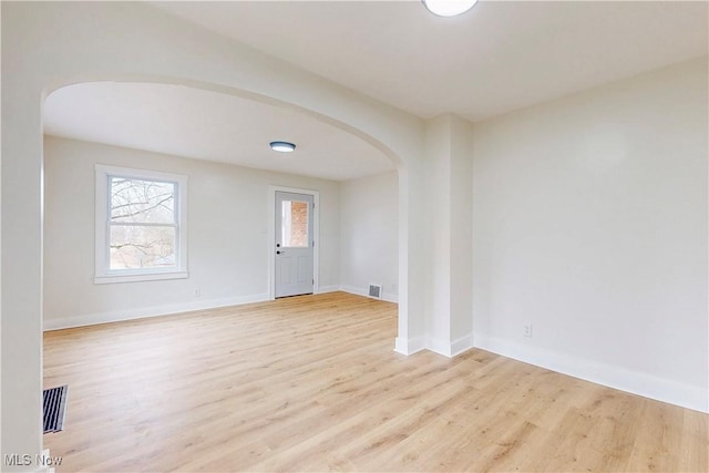spare room with arched walkways, baseboards, visible vents, and wood finished floors
