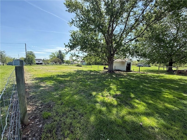 view of yard featuring a rural view, fence, an outdoor structure, and a shed