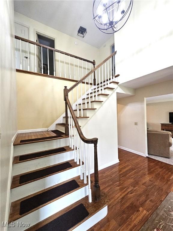 staircase featuring an inviting chandelier, baseboards, a high ceiling, and wood finished floors