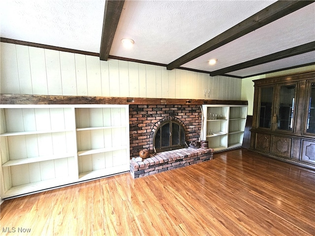 unfurnished living room with wooden walls, a textured ceiling, beamed ceiling, and wood finished floors