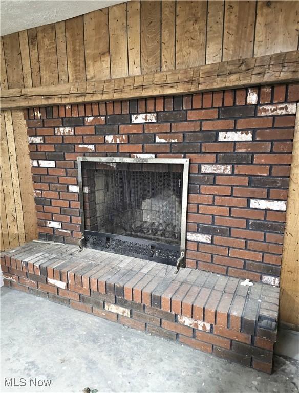 room details with concrete flooring, a brick fireplace, and wood walls