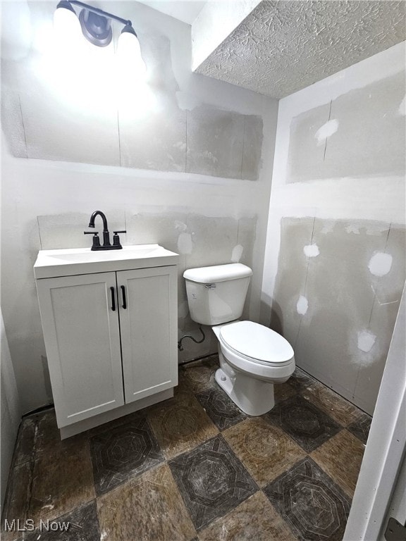 half bath with toilet, a textured ceiling, and vanity