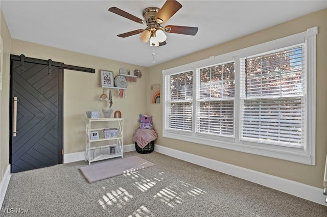 interior space with baseboards, a ceiling fan, carpet flooring, and a barn door