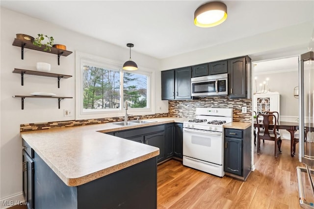 kitchen with white gas stove, tasteful backsplash, a sink, stainless steel microwave, and a peninsula