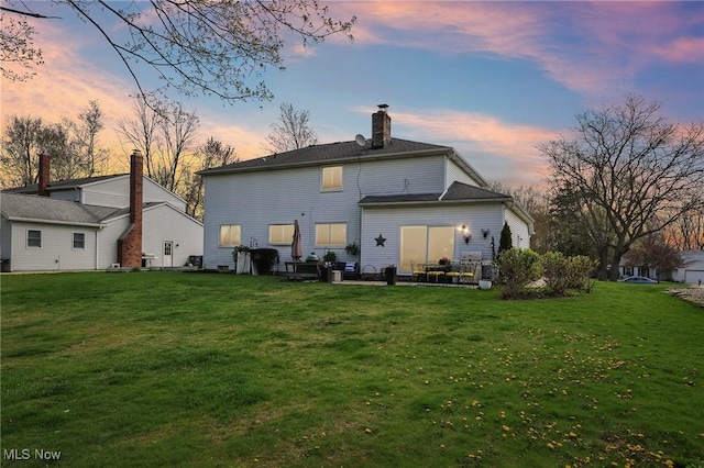 back of property at dusk featuring a lawn and a chimney