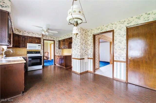kitchen featuring a ceiling fan, white microwave, wallpapered walls, electric range oven, and a sink