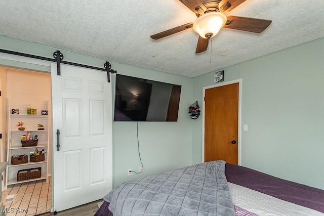 bedroom featuring a ceiling fan, a textured ceiling, and a barn door