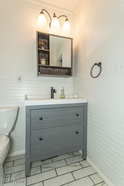 half bathroom with vanity, toilet, and marble finish floor