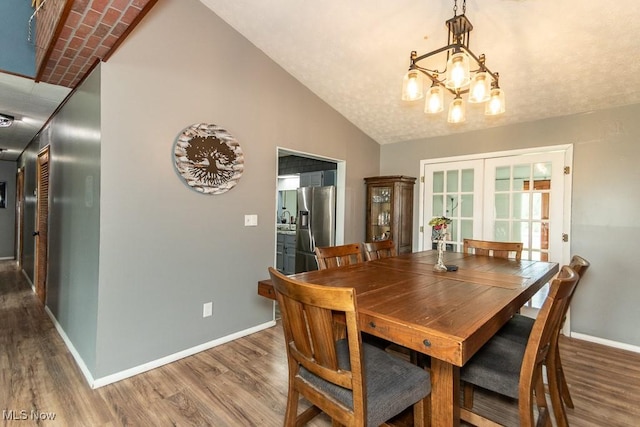 dining space featuring baseboards, lofted ceiling, wood finished floors, and a chandelier