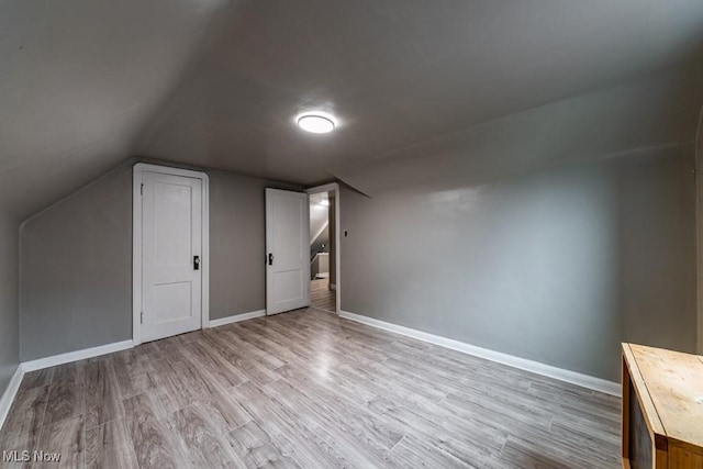 additional living space with light wood-style floors, baseboards, and vaulted ceiling