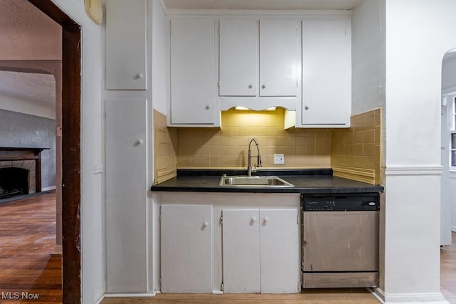 kitchen featuring dark countertops, white cabinetry, tasteful backsplash, a sink, and dishwasher