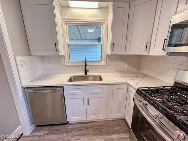 kitchen featuring wood finished floors, white cabinets, light stone counters, a sink, and stainless steel appliances