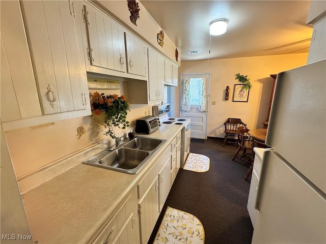 kitchen with a sink, light countertops, a toaster, white appliances, and dark carpet