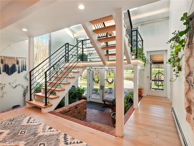 entryway with wood-type flooring, stairs, a towering ceiling, a baseboard heating unit, and french doors