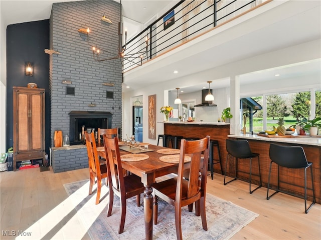 dining room featuring light wood-type flooring, a brick fireplace, and a towering ceiling