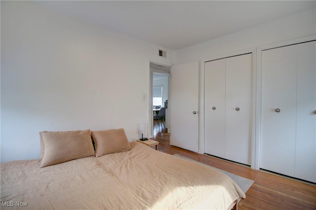 bedroom featuring multiple closets, visible vents, and wood finished floors