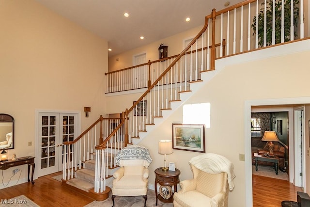 staircase with french doors, a high ceiling, wood finished floors, and recessed lighting