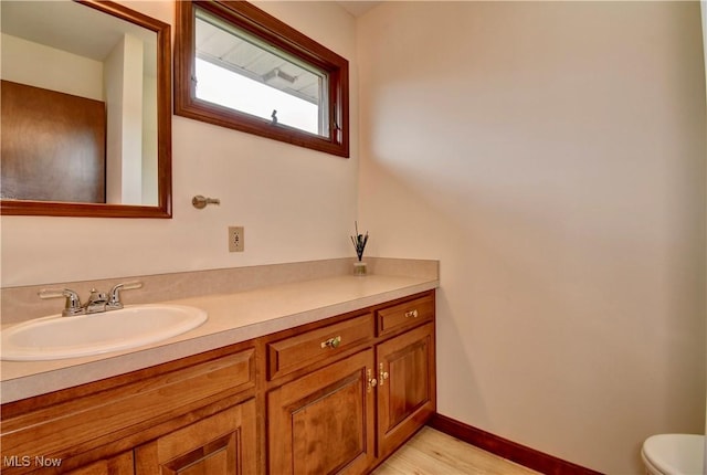 half bathroom featuring toilet, baseboards, wood finished floors, and vanity