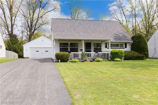 new england style home featuring a detached garage, roof with shingles, covered porch, and a front lawn