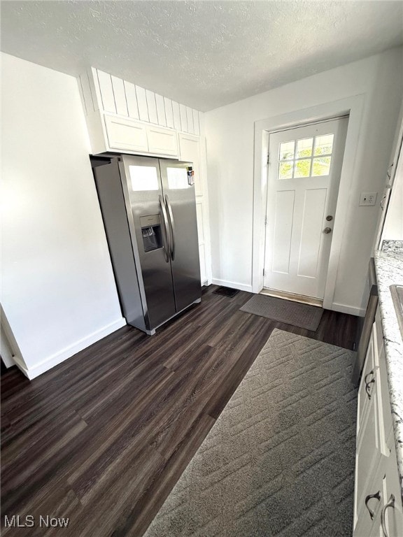 kitchen with a textured ceiling, stainless steel fridge with ice dispenser, baseboards, white cabinets, and dark wood-type flooring