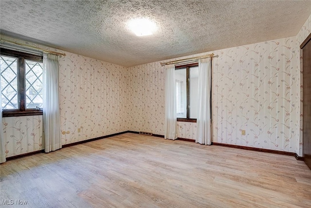 spare room with visible vents, baseboards, wallpapered walls, a textured ceiling, and light wood finished floors