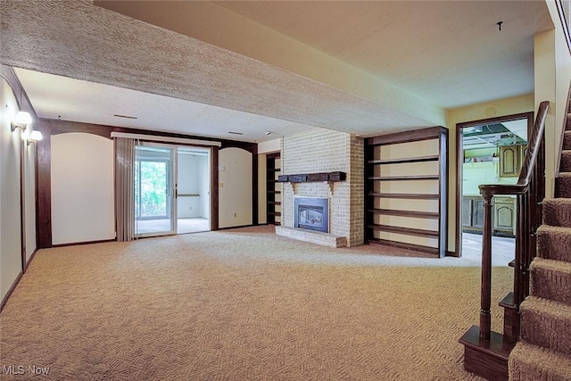 unfurnished living room featuring a textured ceiling, a brick fireplace, stairway, baseboards, and carpet flooring