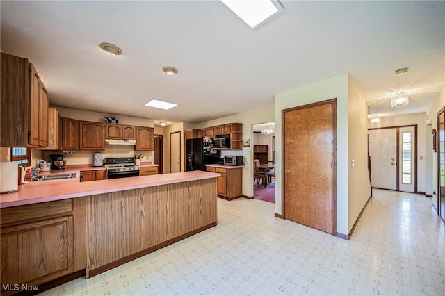 kitchen with a sink, stove, freestanding refrigerator, stainless steel microwave, and under cabinet range hood