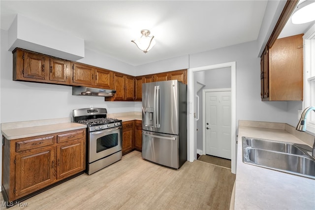 kitchen with a sink, appliances with stainless steel finishes, light wood-style floors, and under cabinet range hood