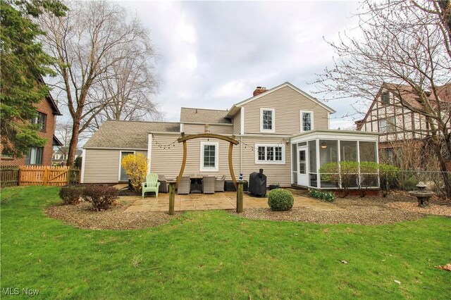 back of house with a chimney, a sunroom, a patio area, fence, and a yard