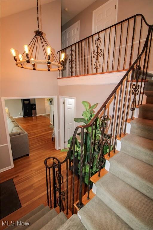 stairway with a high ceiling, wood finished floors, and a chandelier