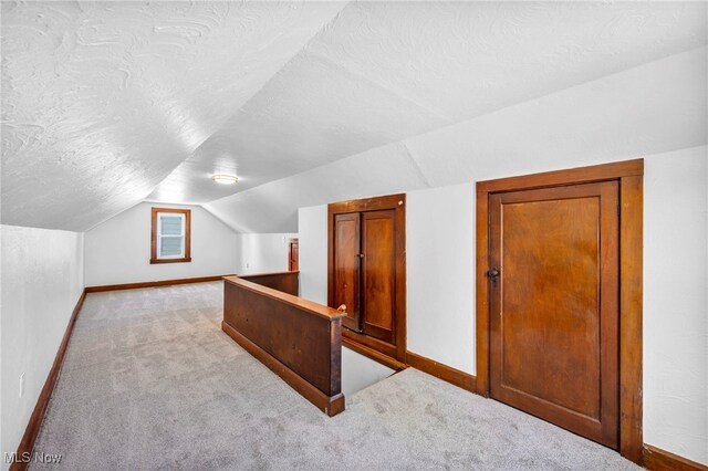 additional living space with baseboards, a textured ceiling, vaulted ceiling, and light colored carpet
