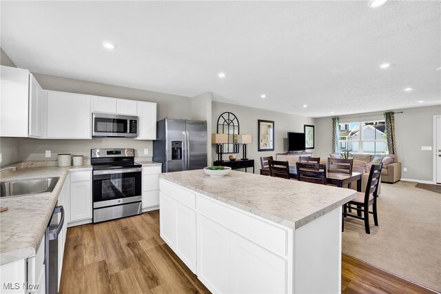 kitchen with a kitchen island, appliances with stainless steel finishes, a sink, light countertops, and open floor plan