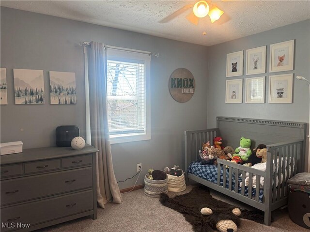 bedroom with a ceiling fan, a textured ceiling, a crib, and carpet