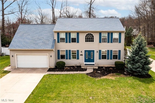 colonial home featuring an attached garage, roof with shingles, driveway, and a front yard