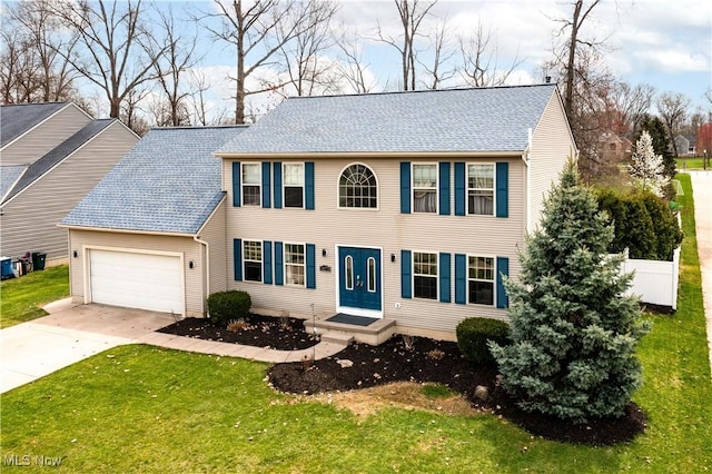 colonial home featuring an attached garage, roof with shingles, driveway, and a front yard