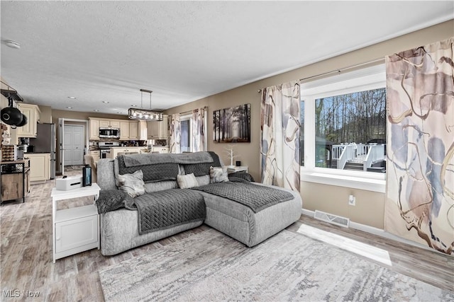 living room featuring visible vents, a textured ceiling, baseboards, and light wood-type flooring