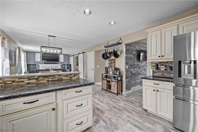 kitchen featuring cream cabinets, a barn door, stainless steel fridge with ice dispenser, open floor plan, and decorative backsplash